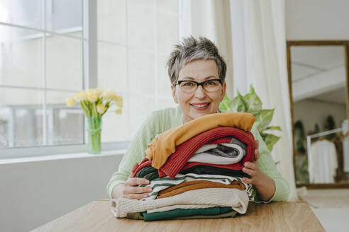 Smiling mature woman with folded clothes at home - YTF01967