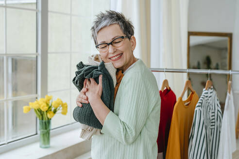 Happy woman hugging clothes at home - YTF01970