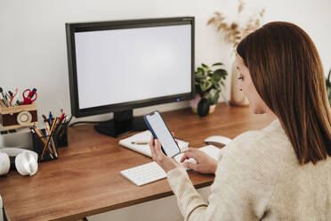 Geschäftsfrau mit Mobiltelefon im Home Office sitzend - EBBF08792