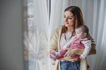 Mutter trägt ihr kleines Mädchen und schaut aus dem Fenster - EBBF08802