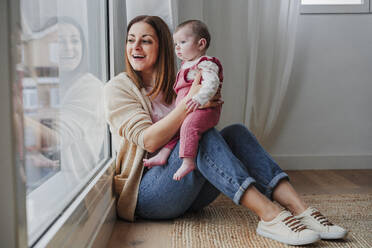 Glückliche Mutter mit Tochter, die zu Hause aus dem Fenster schaut - EBBF08805