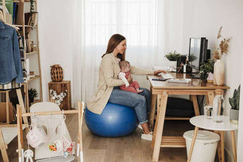 Working mother with daughter using computer at desk - EBBF08815