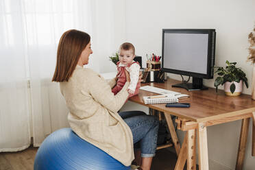 Mother looking at baby girl and sitting on fitness ball - EBBF08822