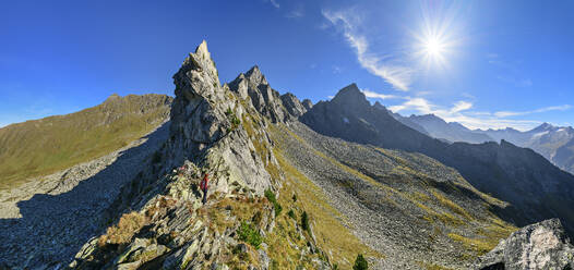 Austria, Tyrol, Sun shining over female hiker following Aschaffenburger Hohenweg trail in Zillertal Alps - ANSF00735