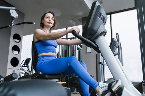 Woman sitting on exercise bike at gym - NDEF01561