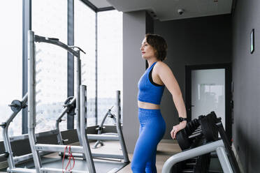 Mature woman standing near exercising equipment at gym - NDEF01566