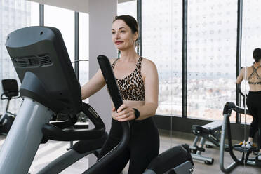 Mature woman doing exercise on elliptical trainer at gym - NDEF01579