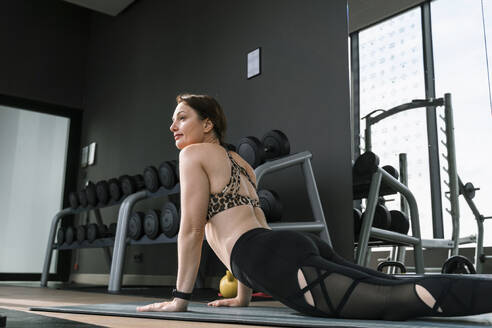 Mature woman doing cobra pose on exercise mat at gym - NDEF01588