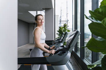 Smiling woman doing cardio training on treadmill at gym - NDEF01593