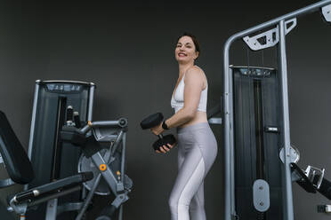 Happy woman doing weight training with dumbbell at gym - NDEF01600