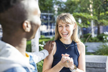 Man with hand on shoulder of woman laughing in city - WPEF08484