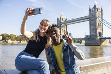 Multiracial friends taking selfie through smart phone with Tower bridge in background - WPEF08490