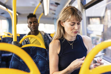 Woman using smart phone sitting with friend in bus - WPEF08518