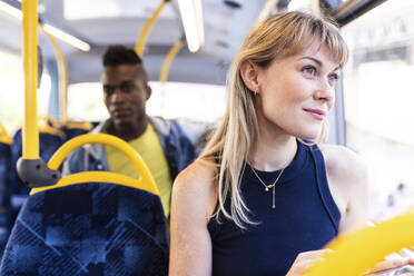 Smiling woman looking out of window sitting with friend in bus - WPEF08519