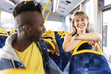 Lächelnde Frau lehnt sich an den Sitz und unterhält sich mit einem Freund, der im Bus sitzt - WPEF08522