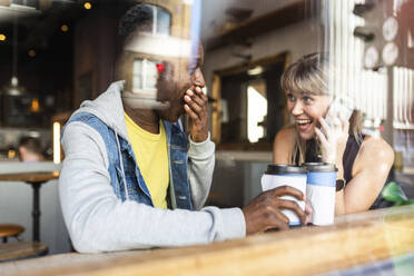 Young multiracial friends having fun at coffee shop seen through window - WPEF08530