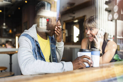 Junge multirassische Freunde, die sich in einem Café amüsieren, gesehen durch ein Fenster - WPEF08530