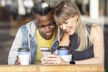 Aufgeregte Freunde teilen sich ein Smartphone im Café - WPEF08539