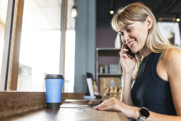 Lächelnde Frau, die in einem Café sitzt und mit einem Smartphone spricht - WPEF08541