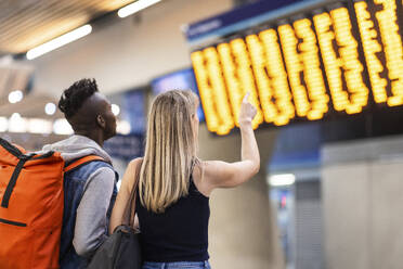 Junge gemischtrassige Freunde überprüfen die Ankunfts- und Abfahrtstafel am Bahnhof - WPEF08548