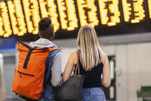 Gemischtrassige Freunde lesen am Bahnhof den Zugfahrplan - WPEF08549