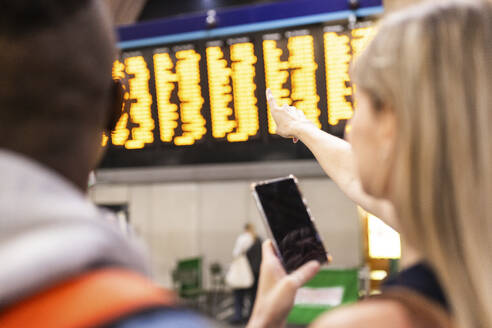 Frau überprüft Zugfahrplan mit Smartphone am Bahnhof - WPEF08550