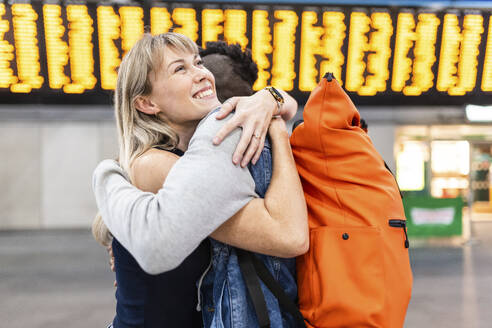 Lächelnde junge Frau umarmt Freund am Bahnhof - WPEF08558