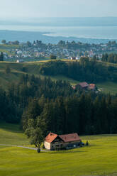 Captivating view of the Appenzell region with rolling hills, a traditional farmhouse, lush forests, and the majestic Lake Constance in the distance, soaked in the golden light of dusk. - ADSF53173