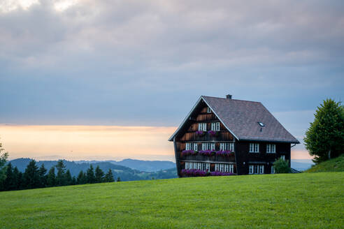 A serene twilight scene featuring a traditional wooden house in the Appenzell region of Switzerland, with lush green grass and a softly lit sky. - ADSF53174