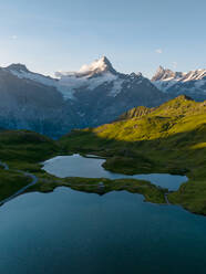 Tranquil alpine lake nestled among rolling green hills with rugged mountains in the backdrop at sunset. - ADSF53190