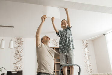 Glücklicher Junge und Vater beim Ablösen alter Tapeten von der Decke zu Hause - ELMF00068