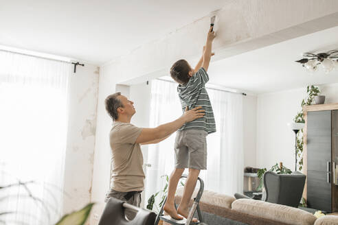 Sohn hilft Vater beim Ablösen alter Tapeten von der Wand zu Hause - ELMF00069