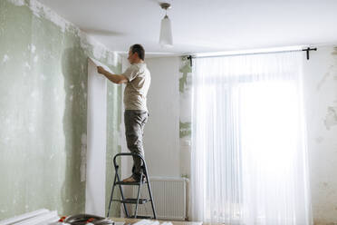 Mann auf Stufenleiter beim Kleben von Tapeten im Wohnzimmer zu Hause - ELMF00086