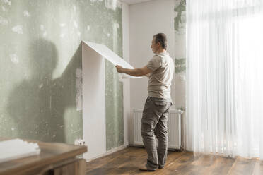 Mann löst alte Tapete von der Wand im Wohnzimmer zu Hause - ELMF00087