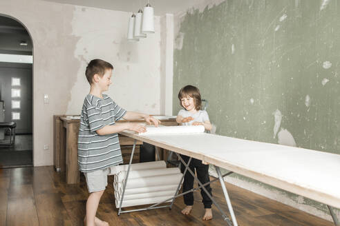Glückliche Brüder rollen Tapeten auf dem Bautisch zu Hause aus - ELMF00088