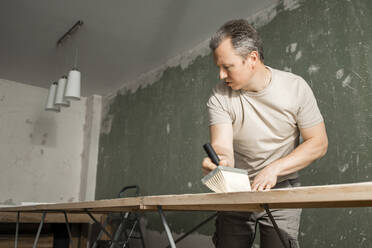 Man applying glue on new wallpaper at workbench in living room - ELMF00091