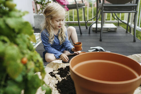 Girl filling pot with dirt in balcony - NSTF00001