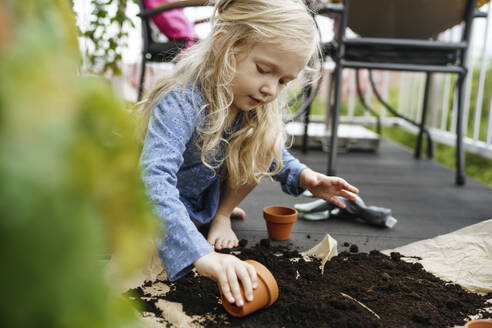 Girl filling pot with dirt and fertilizer in balcony - NSTF00002