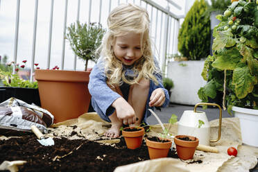 Girl crouching and putting dirt in pots at balcony - NSTF00003