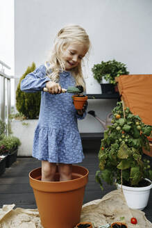 Smiling girl filling dirt in pot with trowel at balcony - NSTF00012