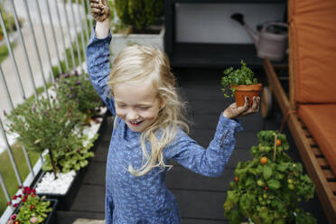 Fröhliches Mädchen hält Pflanze im Balkongarten - NSTF00019