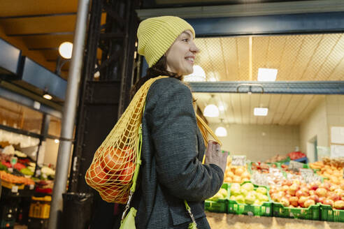 Happy woman with bag of fresh orange fruits in market - OSF02444