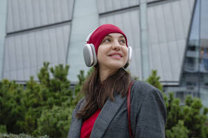 Glückliche junge Frau mit drahtlosen Kopfhörern beim Musikhören - OSF02452