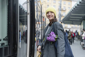 Lächelnde Frau mit Blumen in der Nähe des Zuges - OSF02453