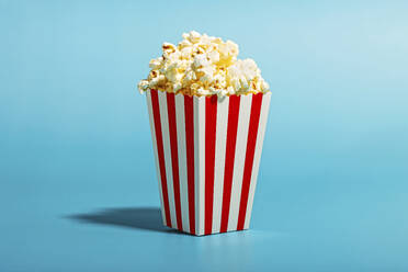 Popcorn in striped container over blue background - RDTF00052