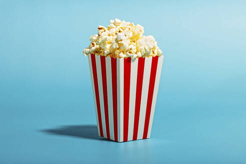 Popcorn in einem gestreiften Behälter auf blauem Hintergrund - RDTF00052