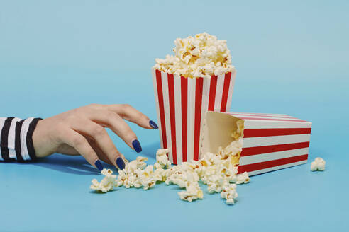 Hand of woman reaching for popcorn over blue background - RDTF00056