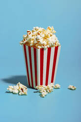 Popcorn in einem rot gestreiften Behälter auf blauem Hintergrund - RDTF00058