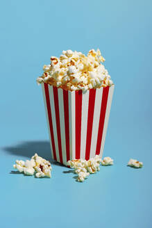 Popcorn in red striped container over blue background - RDTF00058