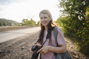Lächelnde Frau hält Kamera an einem sonnigen Tag - EYAF02960
